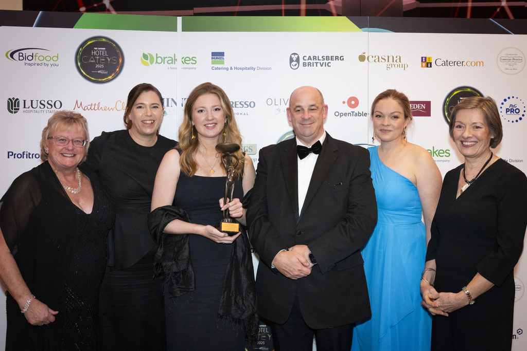 Winners of the Sustainable Hotel of the Year posing with their trophy in front of They Cateys logo wall at an evening awards event.