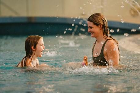 Mother and daughter sat in a pool laughing and smiling